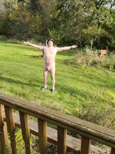 Man standing outdoors with arms outstretched in a natural garden setting, embracing freedom and natu.