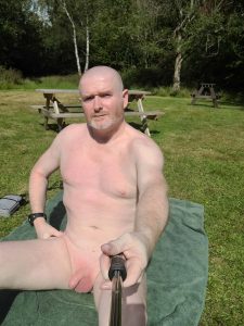 Outdoor man sunbathing with a selfie stick in a park.