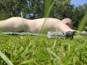 Man lying naked on grass outdoors, enjoying sunbathing in natural surroundings.