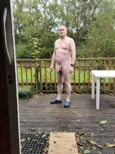 Naked man standing outdoors on a wooden deck with a natural background.